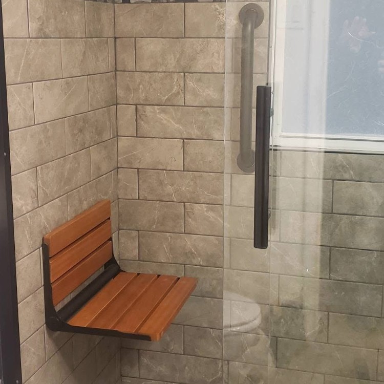 Shower featuring modern gray tile walls, a wooden shower seat, and glass enclosure, showcasing bathroom remodeling by Forge Construction & Design.