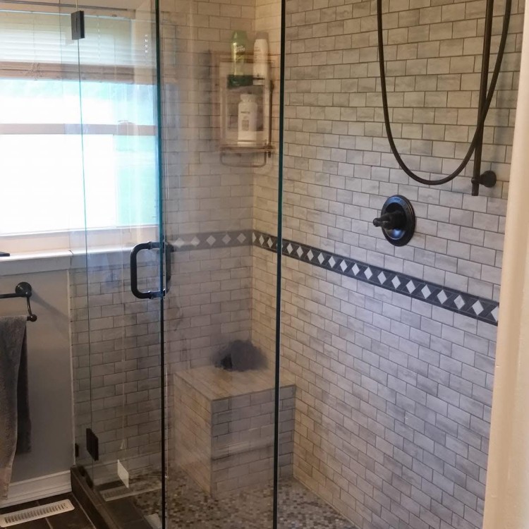 Modern bathroom shower with glass enclosure, tiled walls, decorative border, and built-in shelving for toiletries, showcasing Forge Construction & Design's remodeling capabilities.