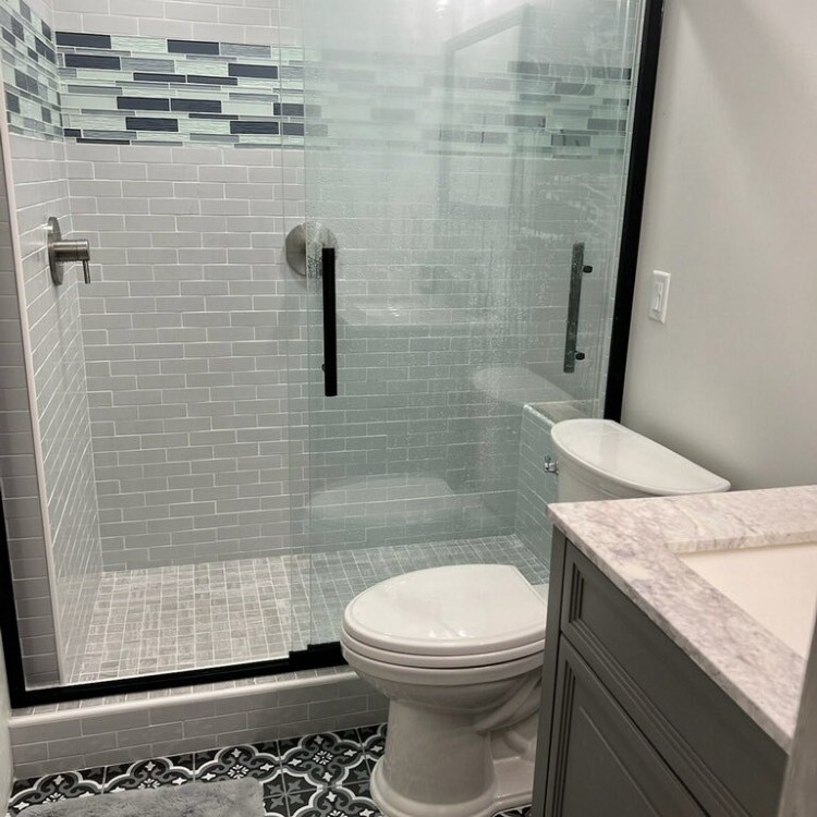Modern bathroom with glass shower enclosure, decorative tile accents, and elegant fixtures, showcasing Forge Construction & Design's remodeling expertise.