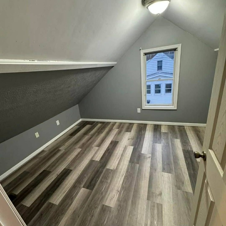 Attic room with sloped ceiling, gray walls, and luxury vinyl flooring, showcasing a window with an exterior view, demonstrating Forge Construction & Design's interior remodeling capabilities.