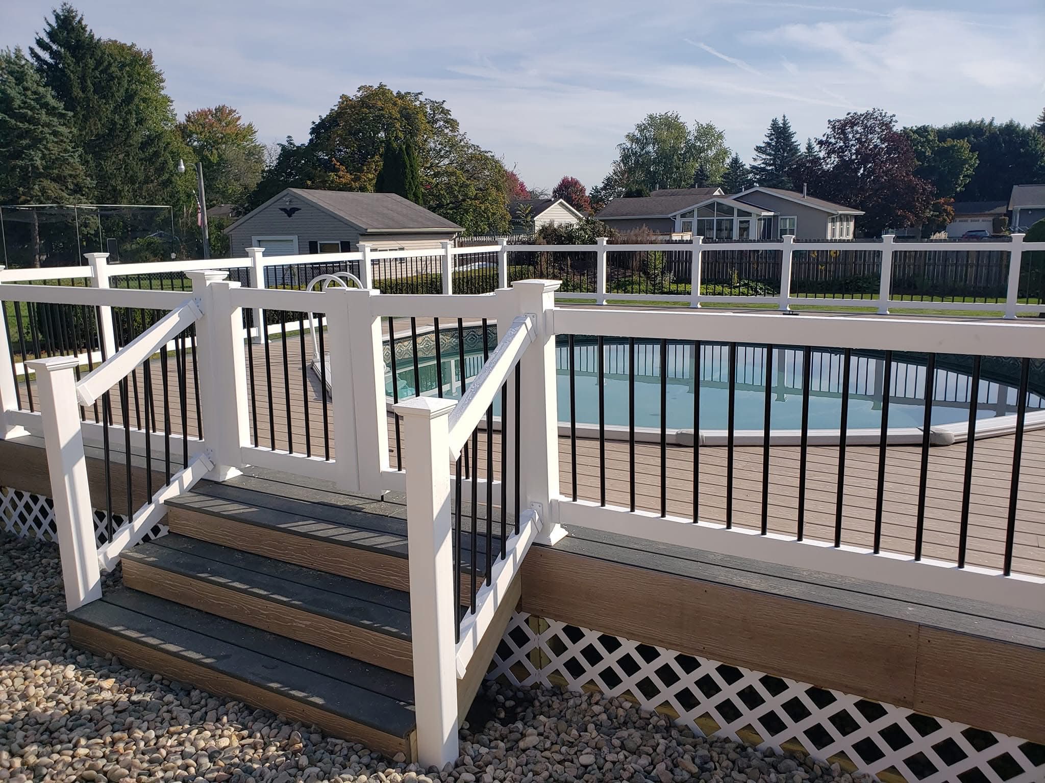 Custom-built deck with white railing and black spindles, leading to an above-ground pool, surrounded by landscaped yard in Northern Indiana.