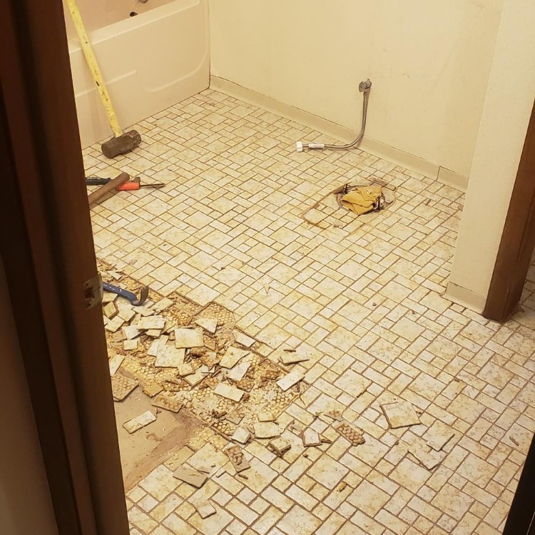 Bathroom floor renovation in progress with scattered tiles and tools, showcasing a custom remodel for Northern Indiana homes.