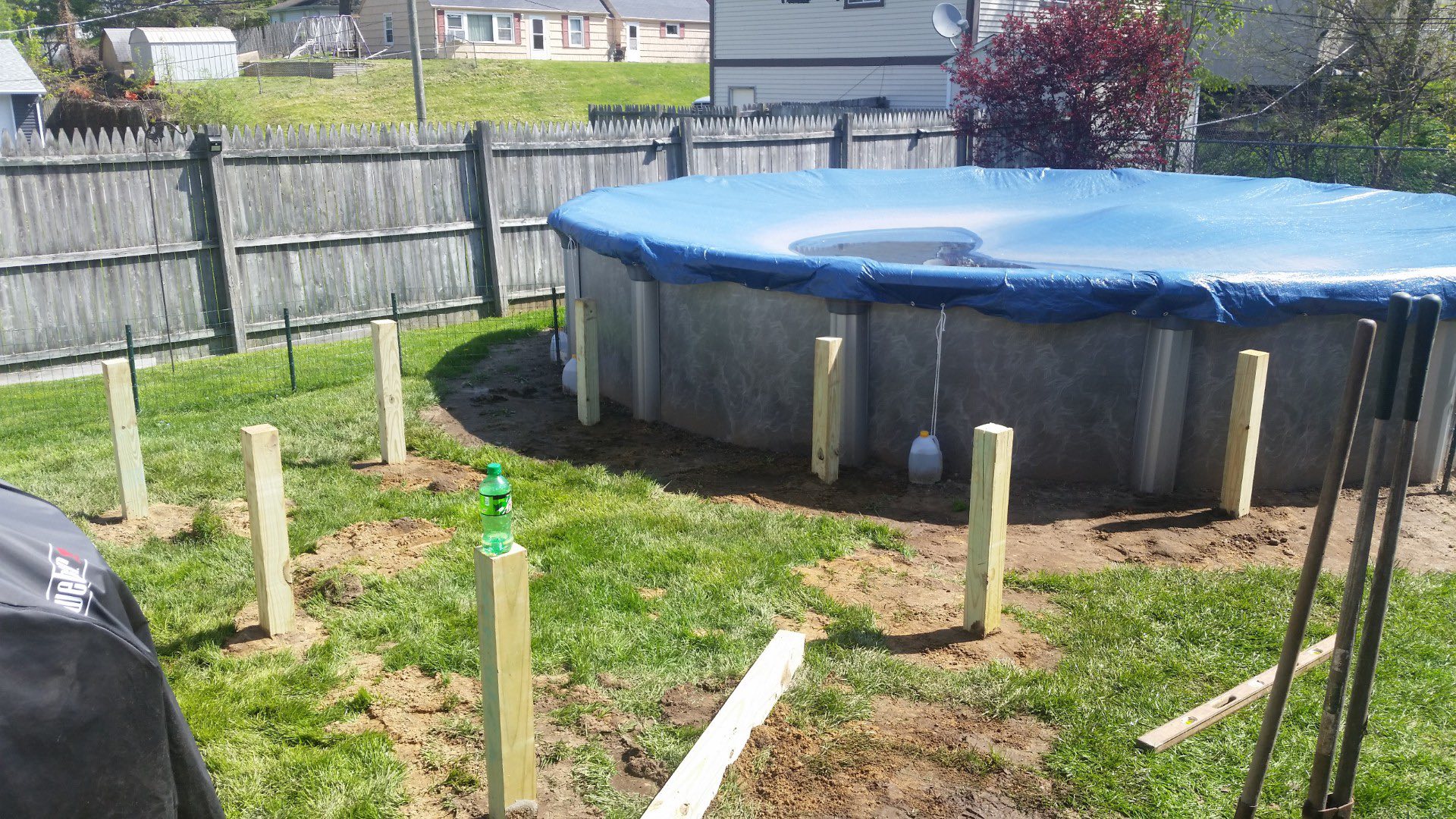 Backyard construction scene featuring a partially assembled above-ground pool with blue cover, surrounded by wooden support posts, grassy area, and tools, illustrating custom outdoor build services by Forge Construction & Design in Northern Indiana.