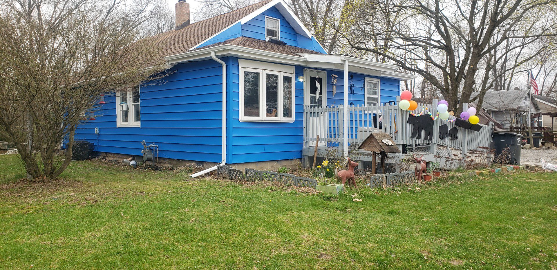 Bright blue house with freshly painted siding, decorative balloons on the porch, and landscaped front yard, showcasing exterior painting services by Forge Construction & Design.